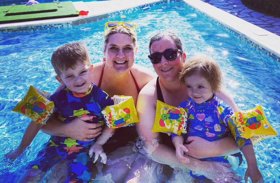 Parents sit in a swimming pool with their twin children
