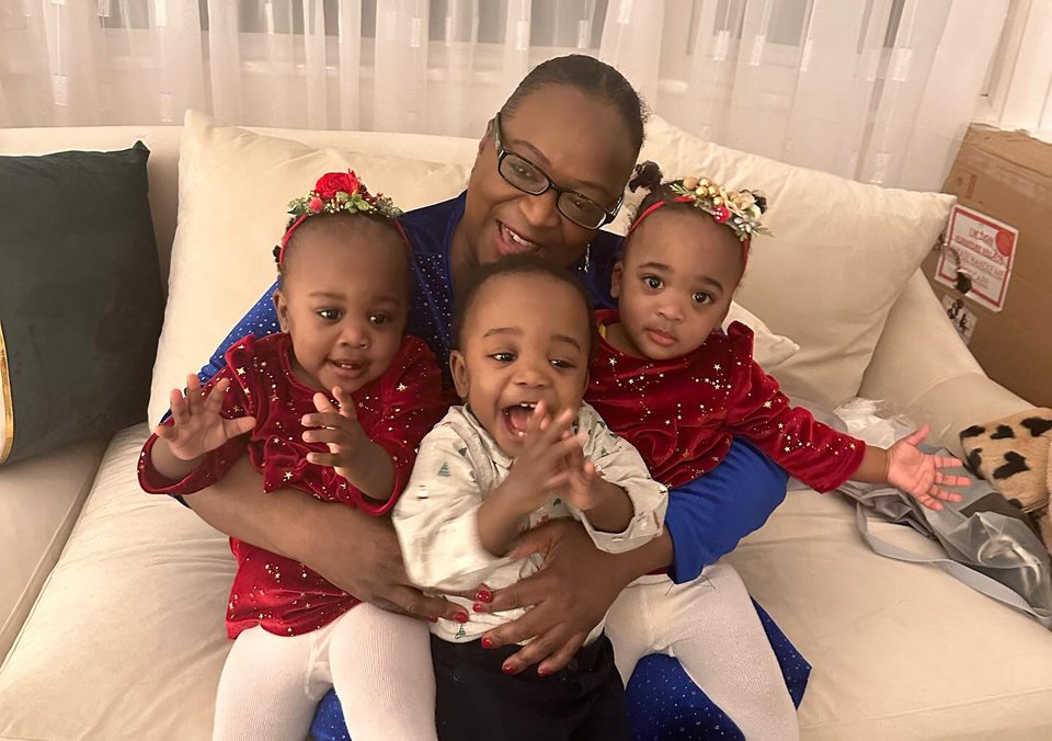A woman sits on a sofa with triplets on her lap