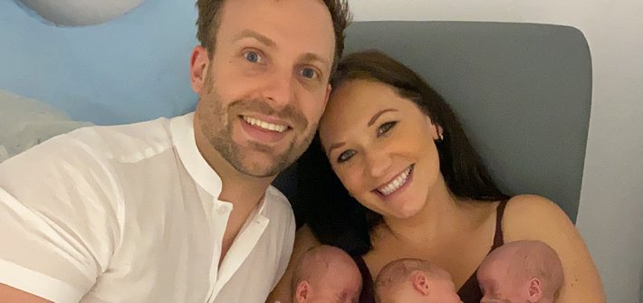 A man and woman sit together with the woman cradling triplet babies