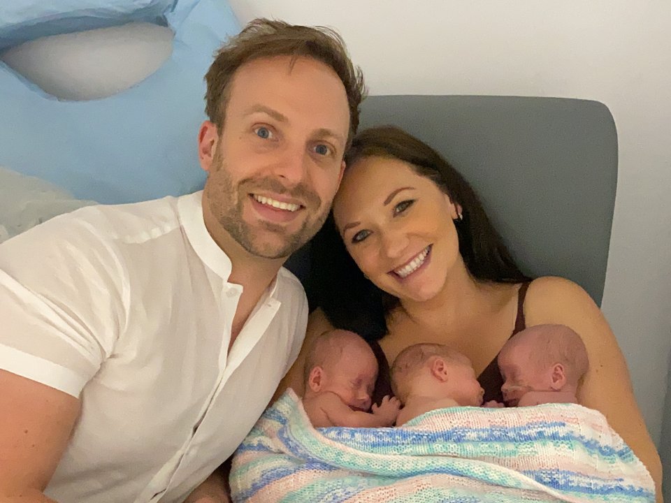 A man and woman sit together with the woman cradling triplet babies