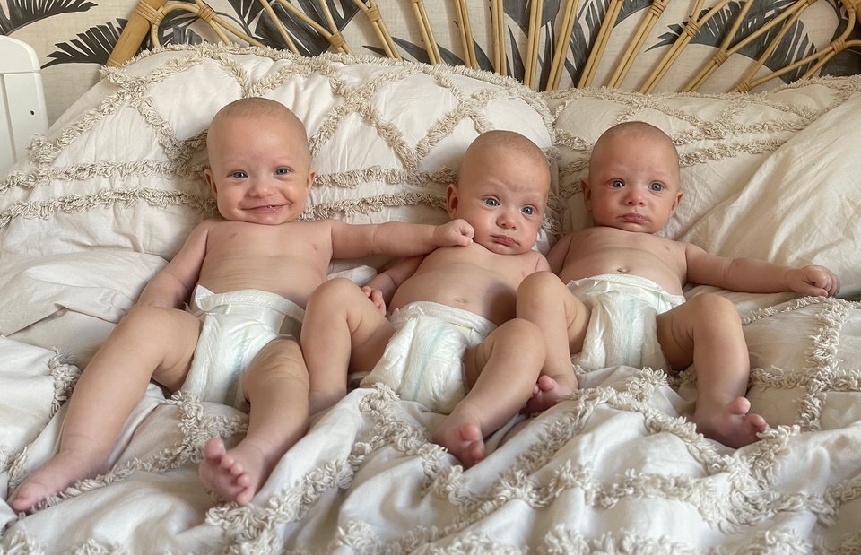 Triplet babies lie next to each other on a bed