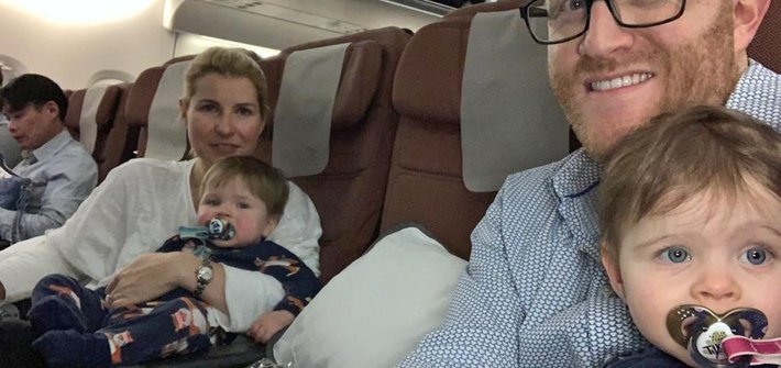 A woman and a man sit in plane seats each holding a toddler