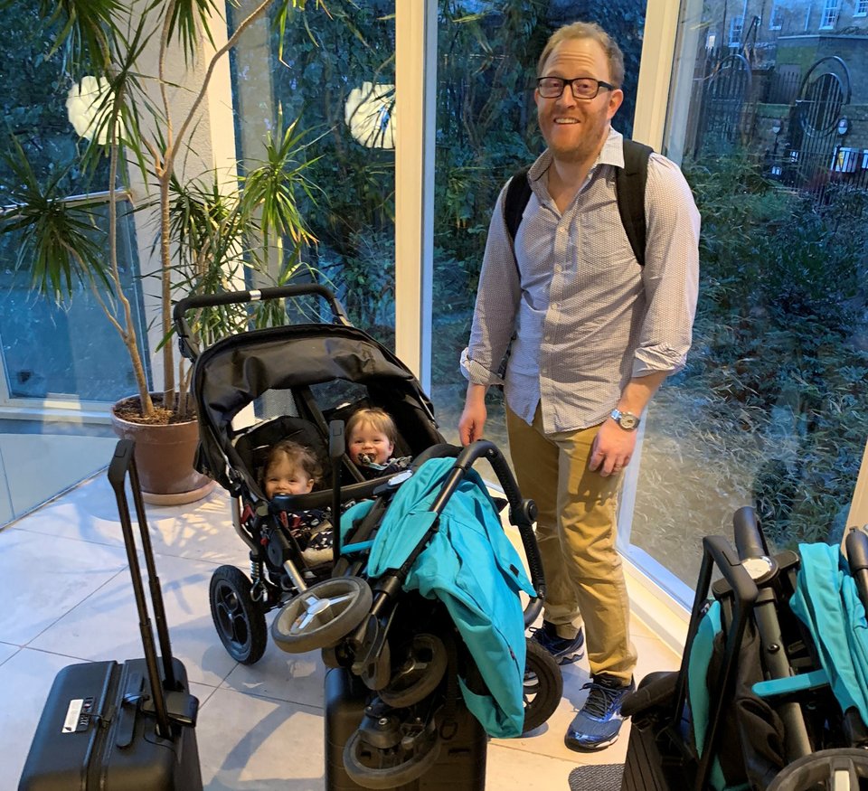 A man stands next to twins in a buggy surrounded by suitcases