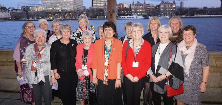 A group of older woman pose together on a terrace in front of a river