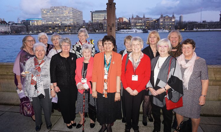 A group of older woman pose together on a terrace in front of a river