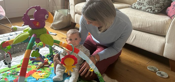 A woman kneels on the floor tending to a baby say on a play mat