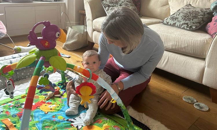A woman kneels on the floor tending to a baby say on a play mat