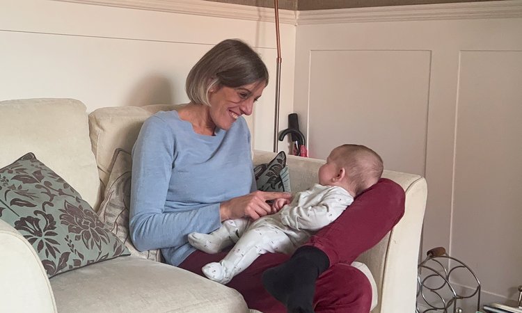 A woman sits on a sofa entertaining a baby in her lap