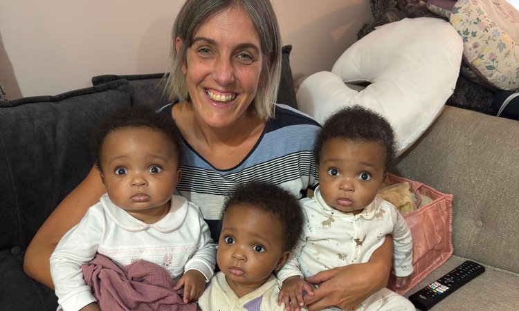 A woman sits on a sofa with young triplets on her lap