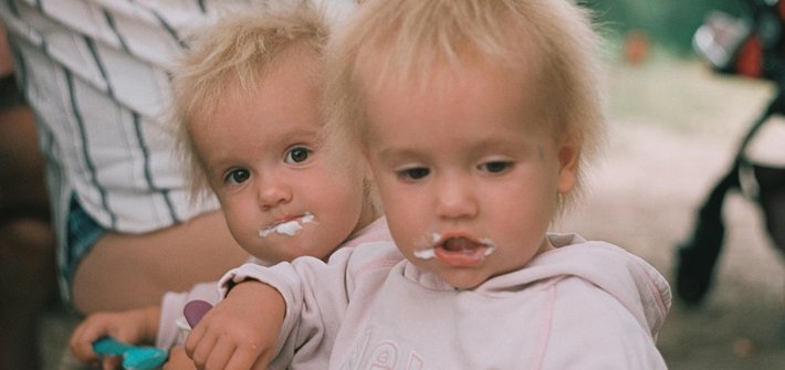 Twins look at the camera with yoghurt around their mouths