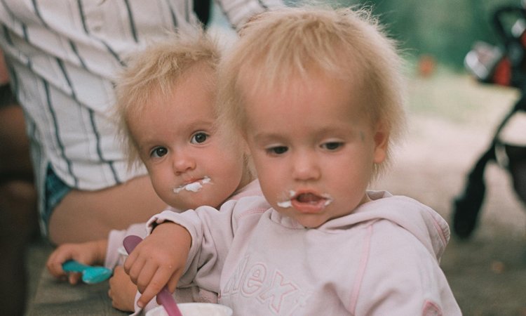 Twins look at the camera with yoghurt around their mouths
