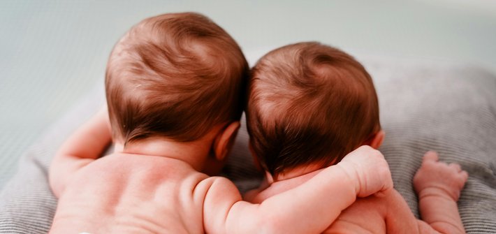 A closeup of two twin babies lying down taken from behind