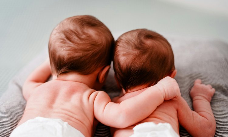 A closeup of two twin babies lying down taken from behind