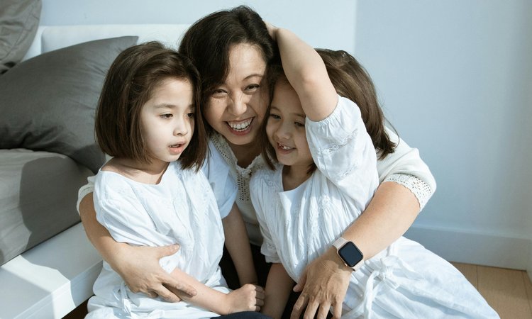 A woman and twin girls hug each other