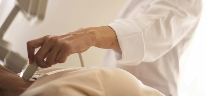 A close-up of a sonography wand on a pregnant belly