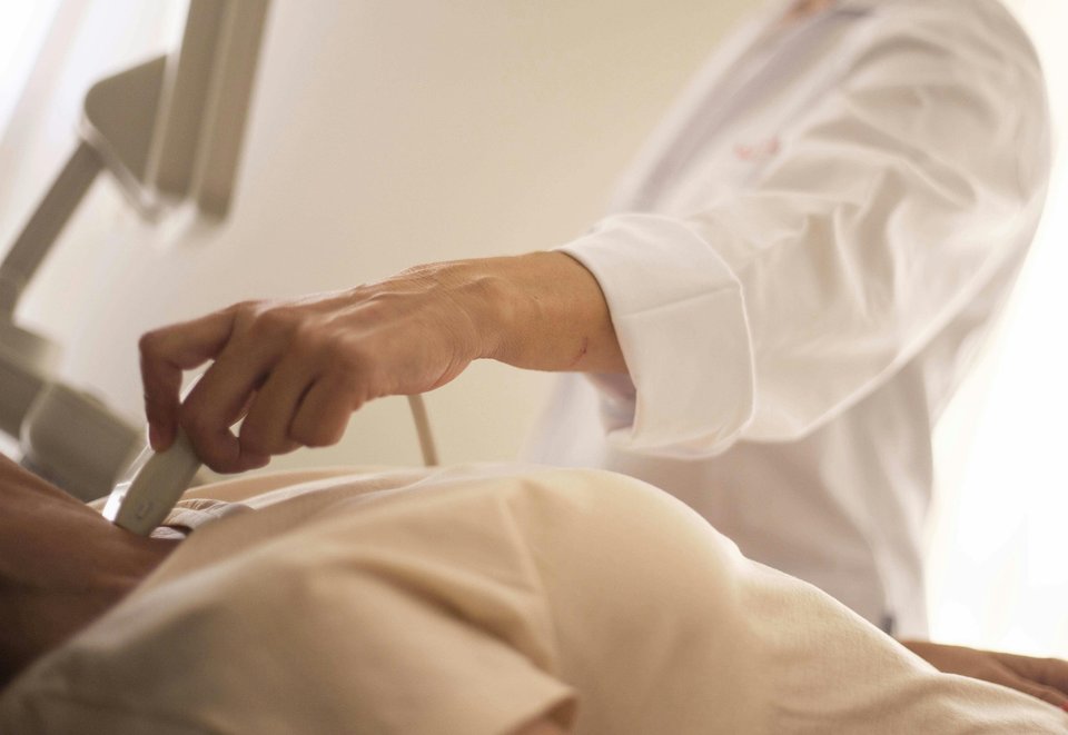 A close-up of a sonography wand on a pregnant belly