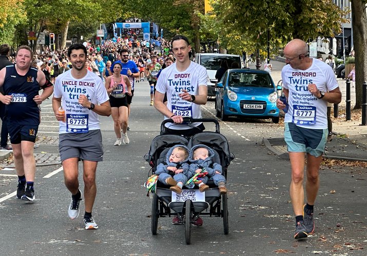 Three men in Twins Trust t-shirts running in a charity race with one pushing a double buggy with twins sitting in it