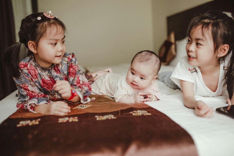 asian sisters having fun with newborn baby on bed