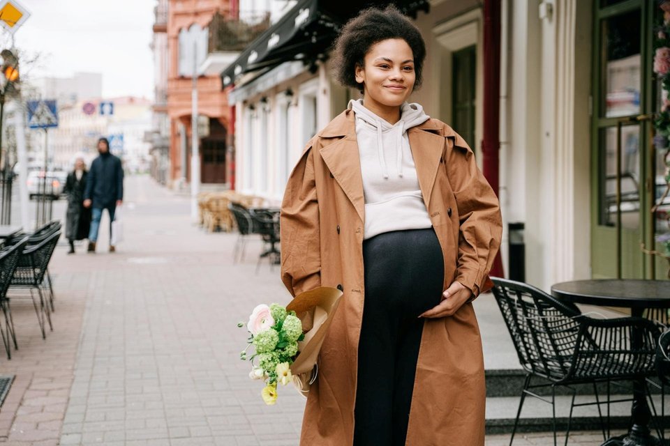 a pregnant woman holding a bouquet of flowers walking down the street