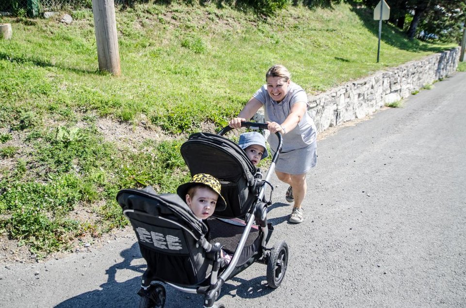 a woman struggling to push a double stroller up a hill