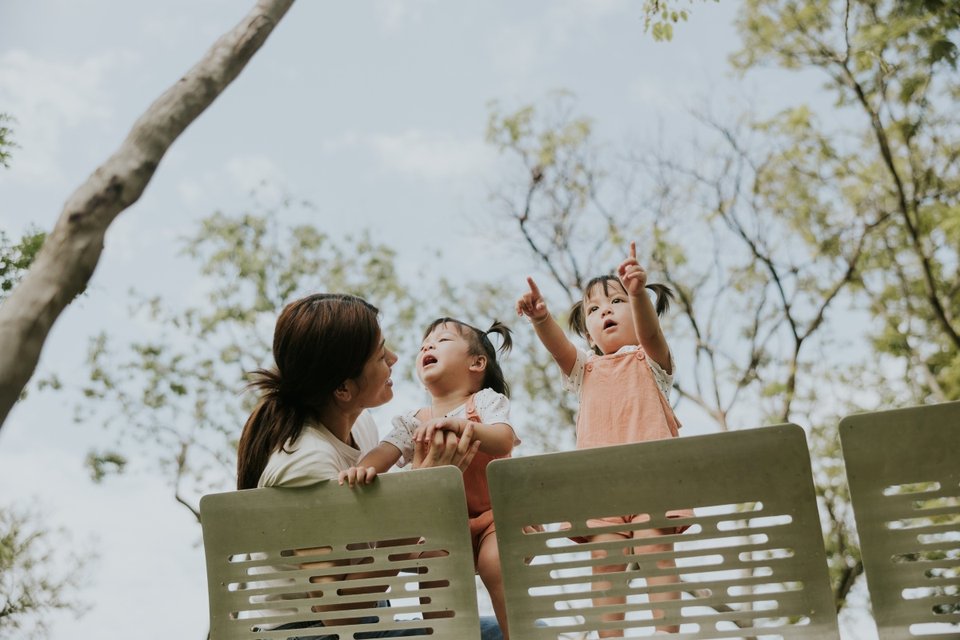 an Asian mother with her twin girls on a park bench