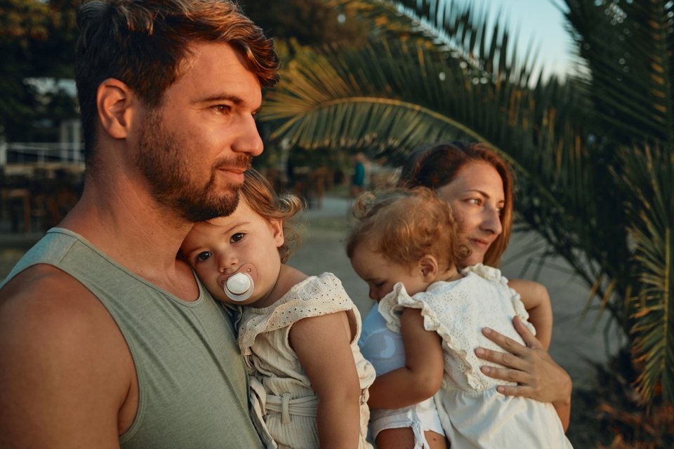 mother and father holding a twin toddler each watching the sunset