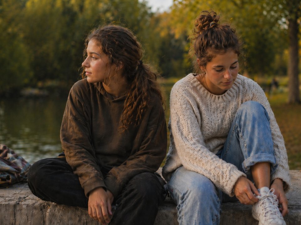 twin teenage girls dressed differently sat in a park