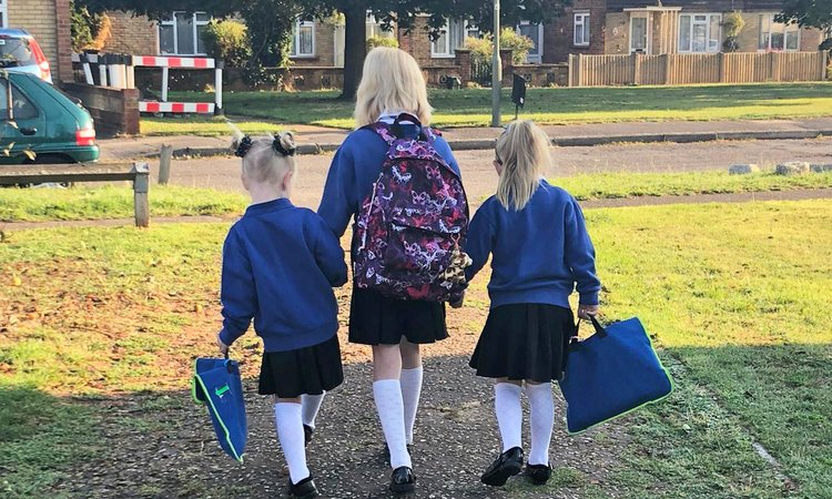 Twin girls dressed in school uniform walk either side of an older girl in school uniform holding hands