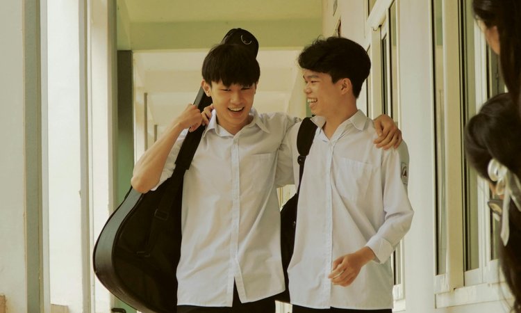 Two secondary school ages boys walk down a corridor in school uniform with arms around each other joking
