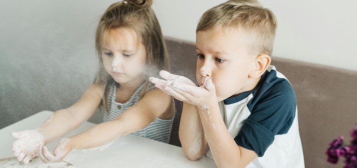 A boy and girl sit next to each other playing with flour