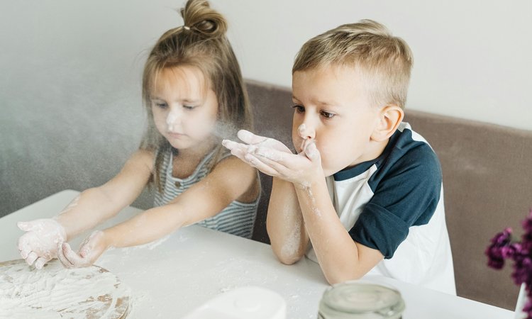 A boy and girl sit next to each other playing with flour