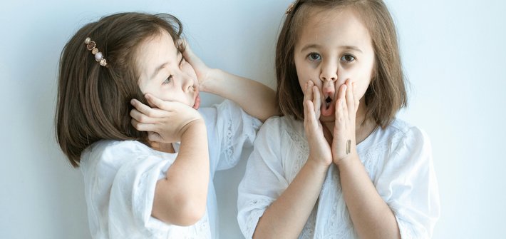 Twin girls stand next to each other pulling faces with their hands