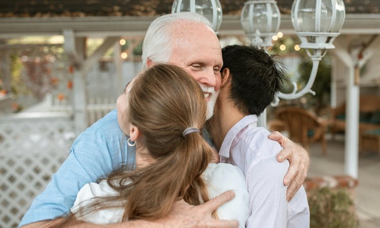 An elderly man hugs a younger man and woman