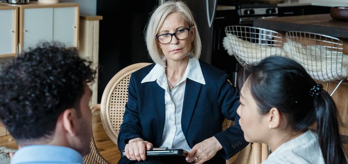 A woman sits watching a couple in the foreground with their backs to the camera explain something