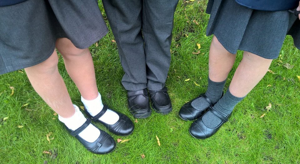 A close up of three pairs of school shoes being worn