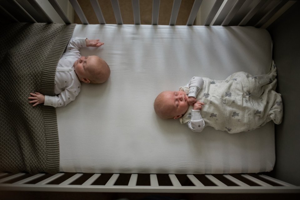 twin babies sleeping on either end of a baby cot