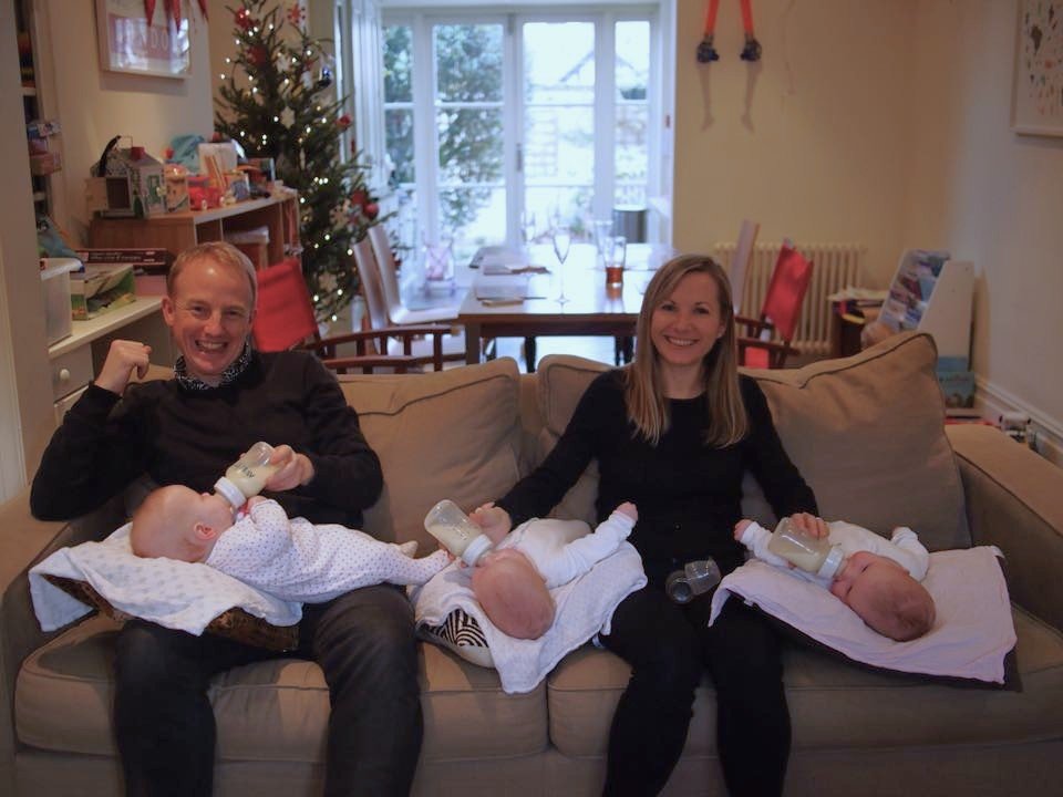 a man and a woman bottle feeding triplet babies on a sofa