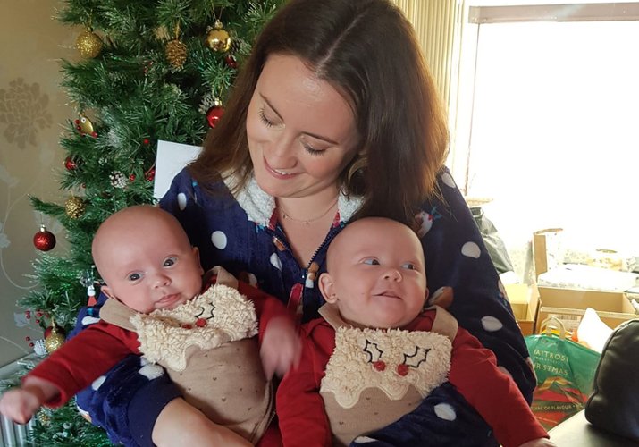 A woman looks down on twin babies she holds in her arms