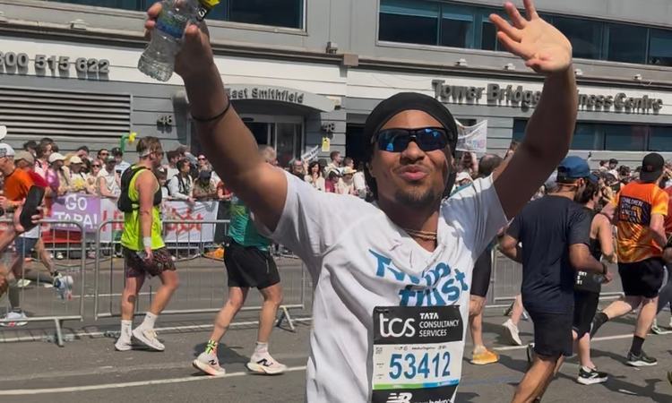 A man turns to wave at the camera whilst running in the London Marathon