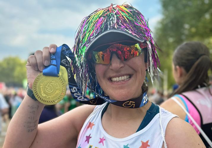 A woman smiles at the camera holding up a London Marathon finishers' medal next to her