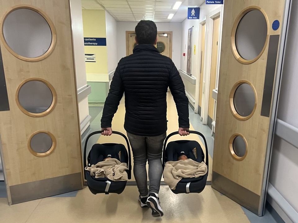 a man holding two car seats walking away in a hospital
