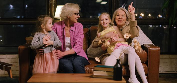 Two older woman sit on a sofa each with a you girl on their lap