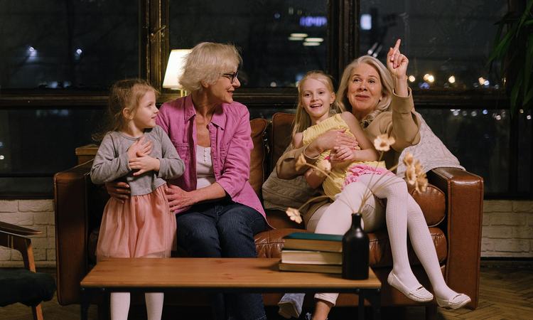 Two older woman sit on a sofa each with a you girl on their lap