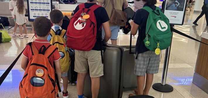 five young children and a man waiting to check-in at the airport