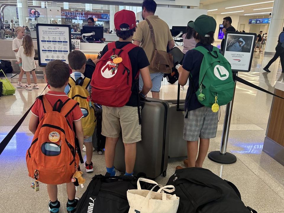 five young children and a man waiting to check-in at the airport