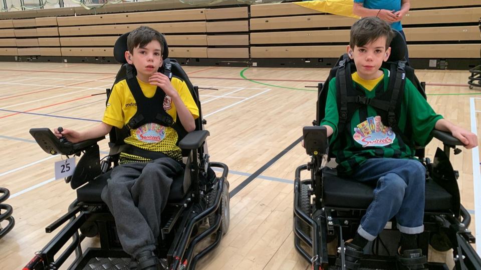 two boys sat in electric wheelchairs in a gymnasium