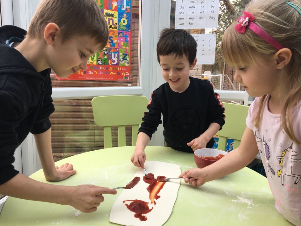 two boys and a girl spreading tomato sauce on a pizza base