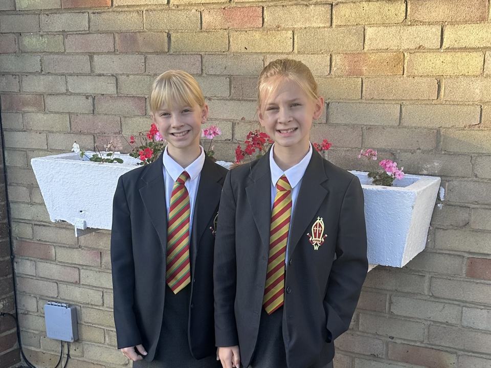 two twin girls in school uniform smiling