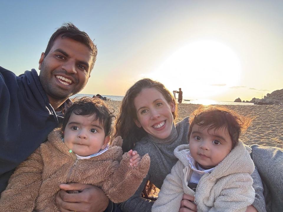 a father and a mother with their twin children on a beach during sunset
