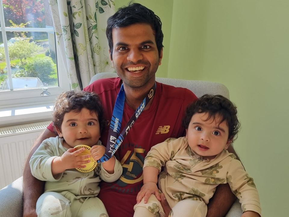 a man wearing a runners' medal holding twin babies